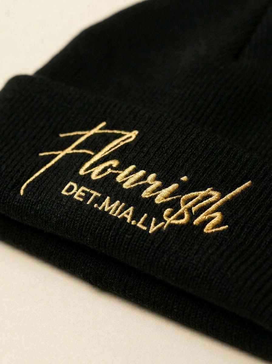 Macro close-up of the gold Flouri$h cuff embroidery on the beanie's chunky rib knit