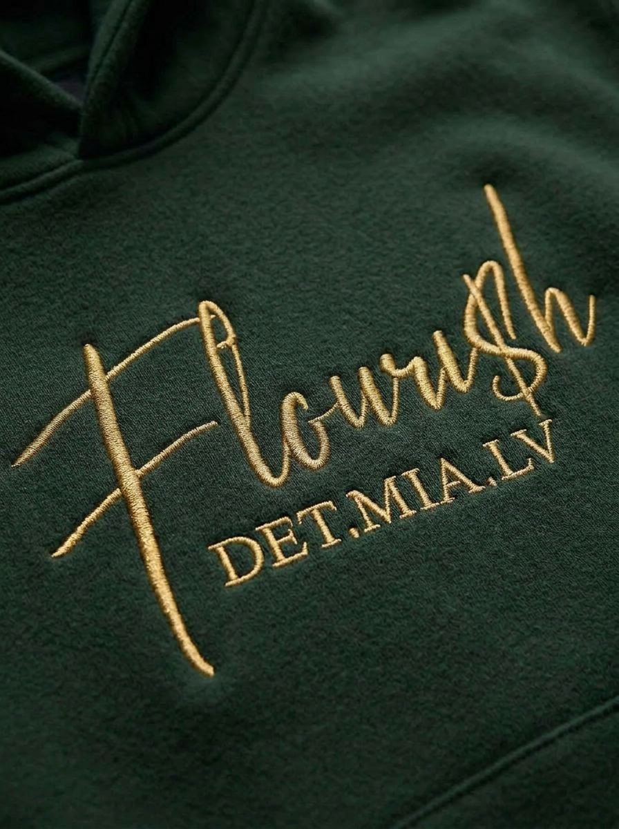 Macro close-up of the gold Flouri$h script embroidery on the hoodie chest
